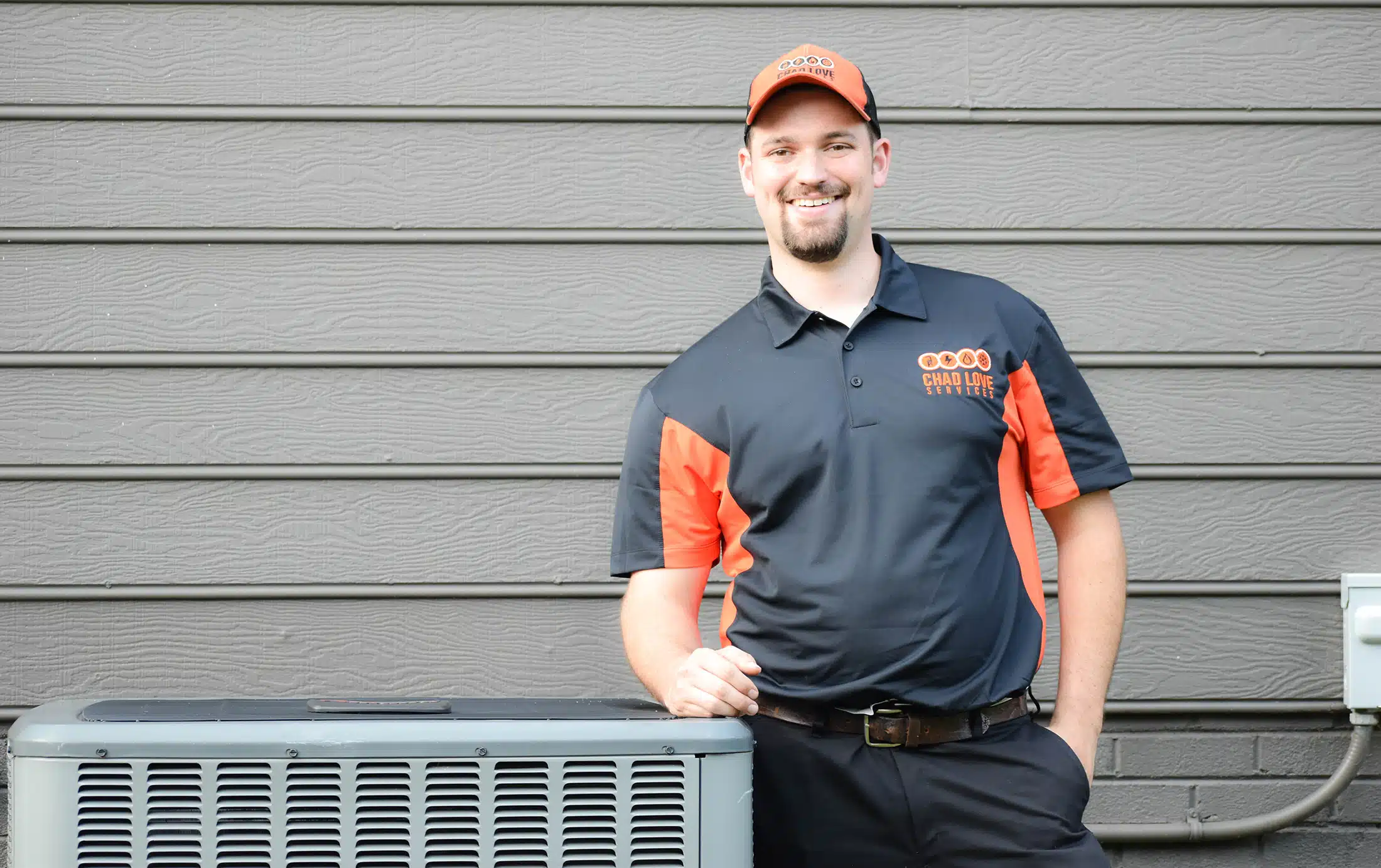 Chad Love Services tech smiling and leaning on AC outside of residential home in Concord, NC.